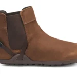 A brown ankle-high leather Chelsea Boot from Xero Shoes featuring a pull tab at the back, elastic side panel, and dark rubber sole. This stylish design also includes a small strap detail near the heel for added flair.